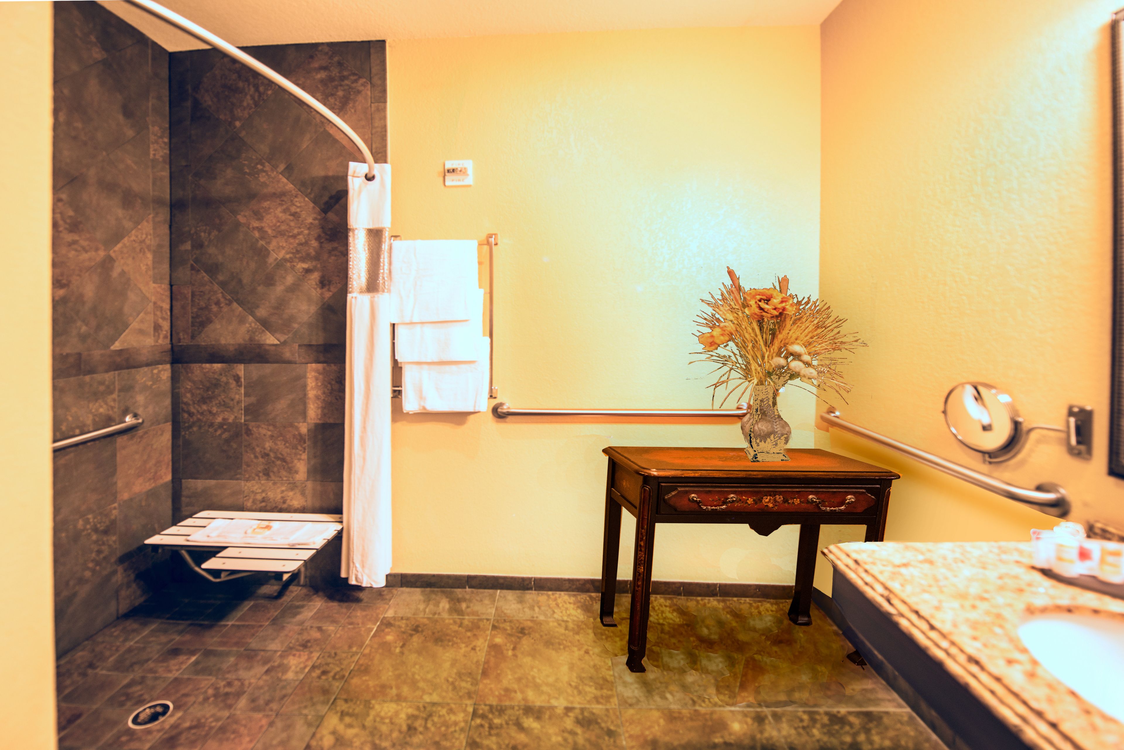 Une salle de bain avec une douche, un meuble-lavabo avec un évier et un vase rempli de fleurs posé sur le meuble-lavabo.