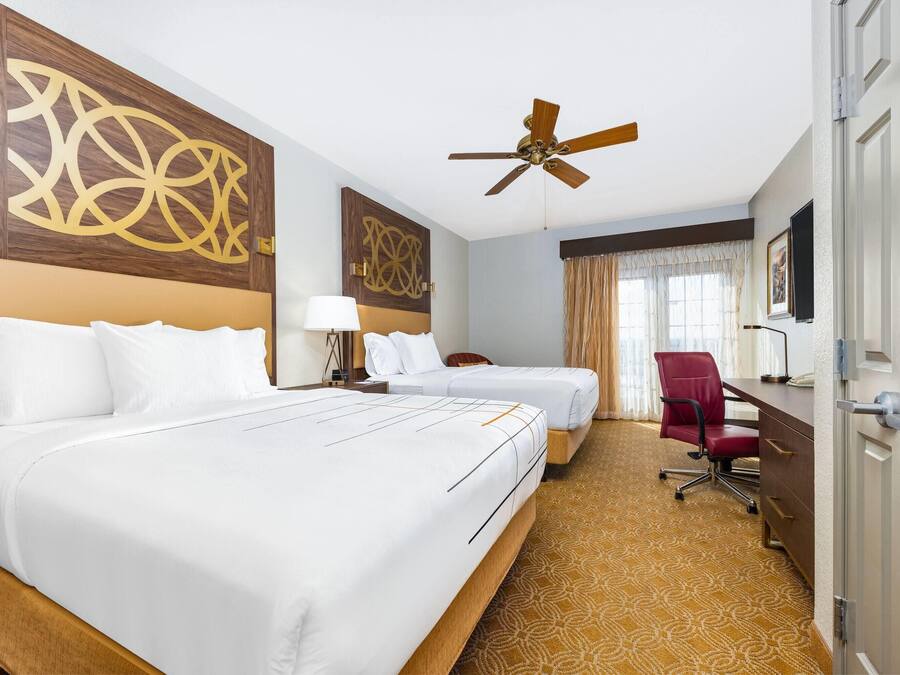 Ein Hotelzimmer mit zwei Betten, einem Schreibtisch, einem Stuhl, einem Deckenventilator und einem großen Wandbild.