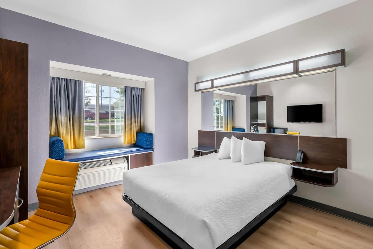 Ein modernes Hotelzimmer mit einem großen Bett, einer Sitzecke am Fenster, einem Flachbildfernseher und einer fest installierten Heizung.