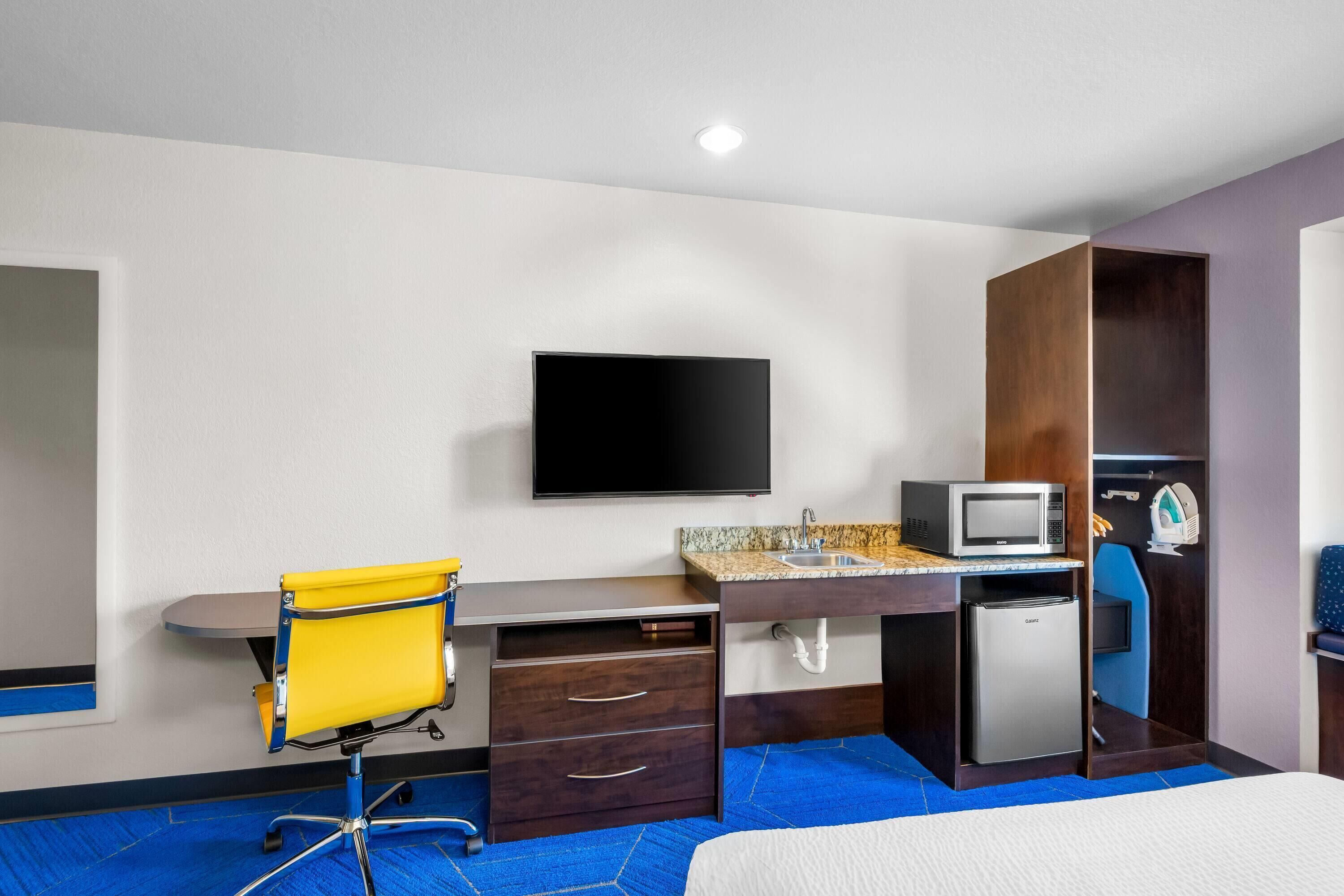 Habitación de hotel con cama, escritorio con silla, televisor, microondas, refrigerador pequeño y armario.