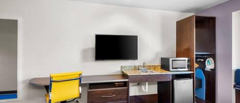 Habitación de hotel con cama, escritorio con silla, televisor, microondas, refrigerador pequeño y armario.