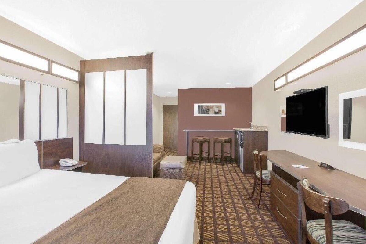 Habitación de hotel con cama, escritorio, silla, televisión y una pequeña zona de kitchenette.
