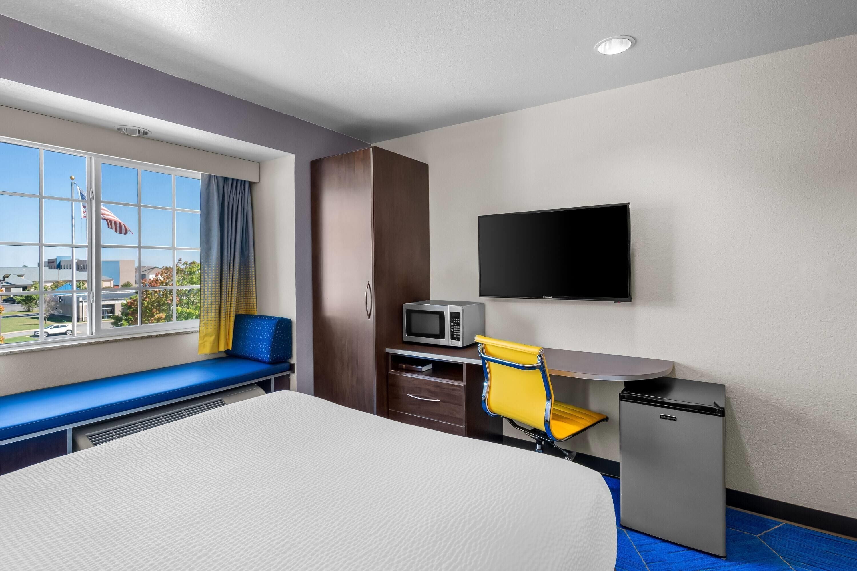 A hotel room with a bed, a desk with a chair, a television, a microwave, and a small refrigerator.