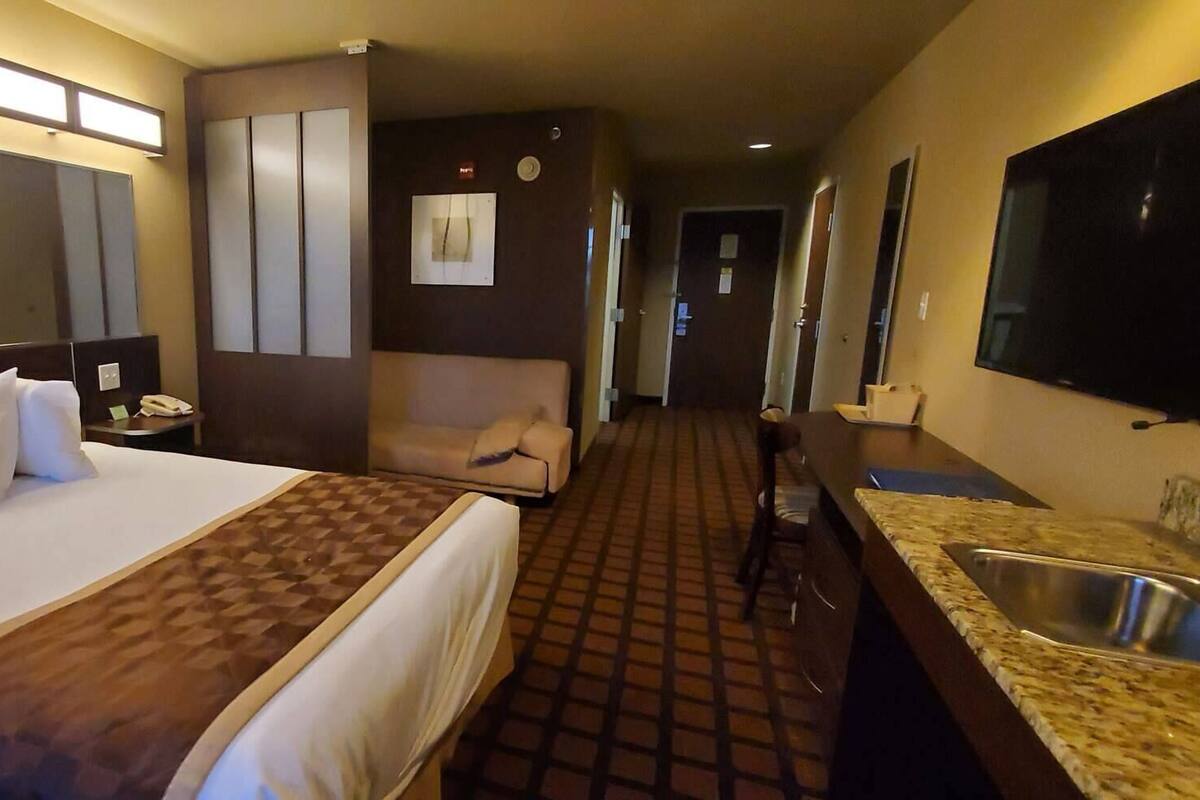 Ein Hotelzimmer mit einem Bett, einem Schreibtisch, einem Sessel, einem Waschbecken und einem Fernseher.