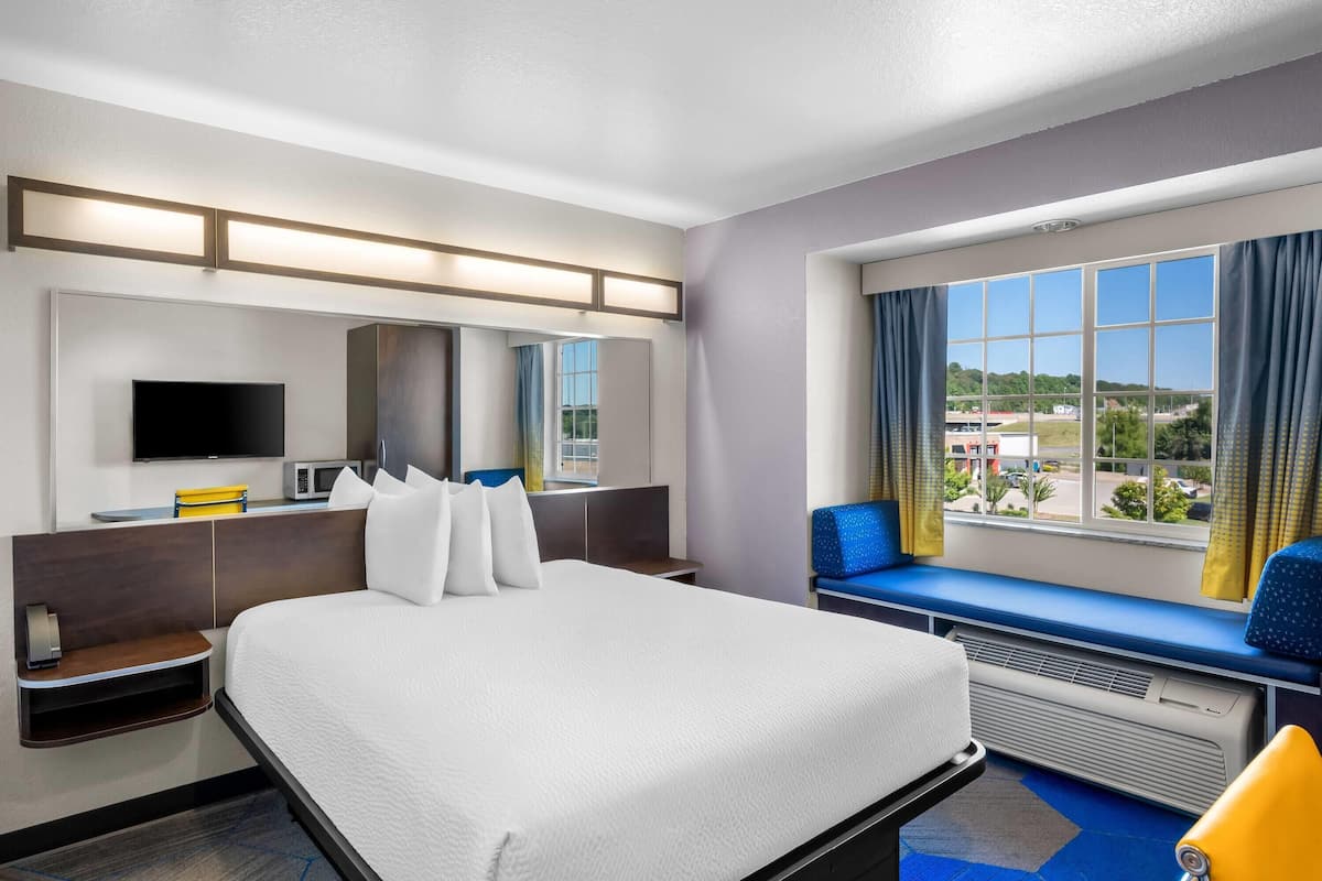 Ein Hotelzimmer mit einem grossen Bett, einem Flachbildfernseher, einer Mikrowelle und einem Fenster mit Blick nach draussen.