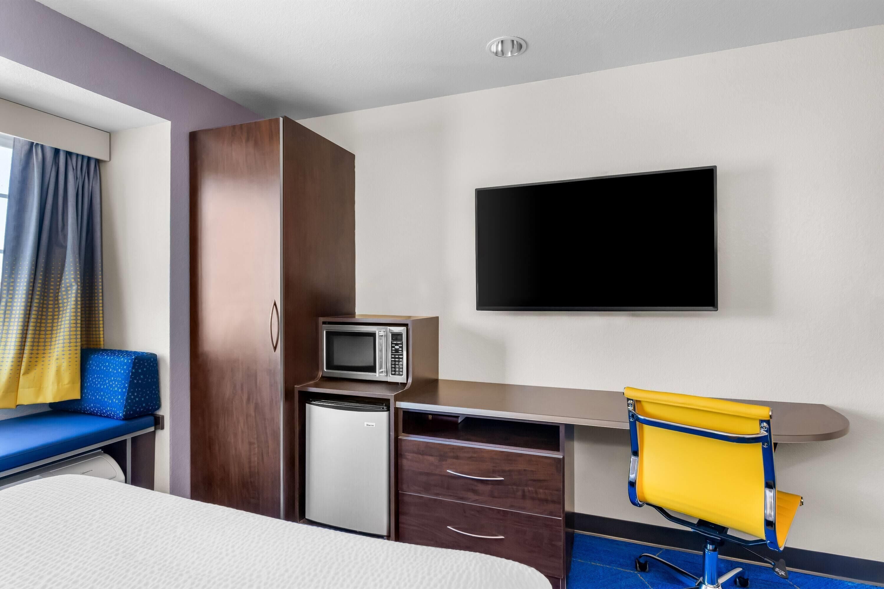 A hotel room with a bed, a desk with a chair, a television, a microwave, and a small refrigerator.