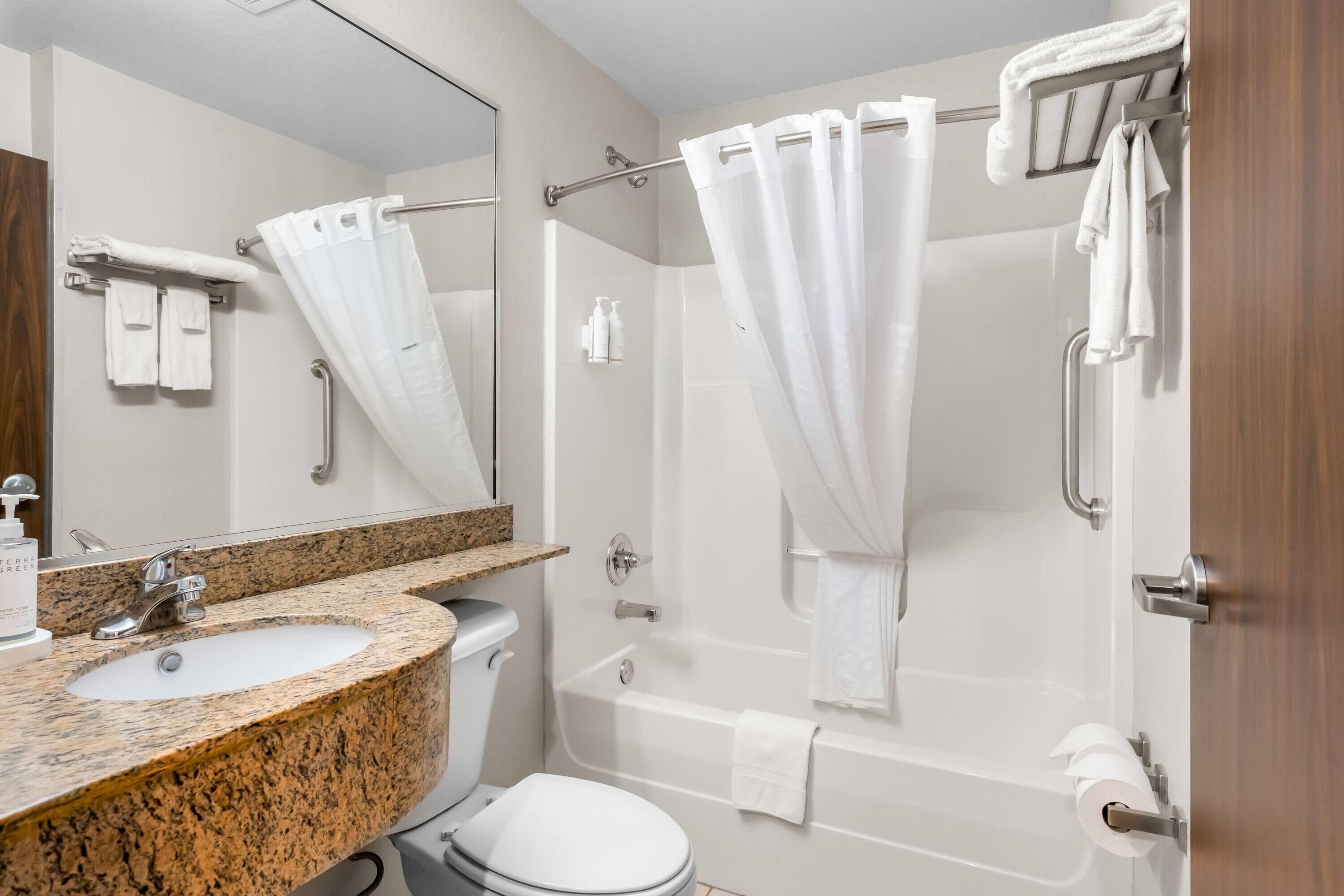 Un baño moderno con lavamanos de granito, inodoro, bañera y cortina de ducha.