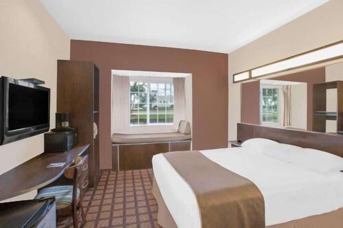 Una habitación de hotel con una cama, televisión, escritorio y ventana con vistas al exterior.