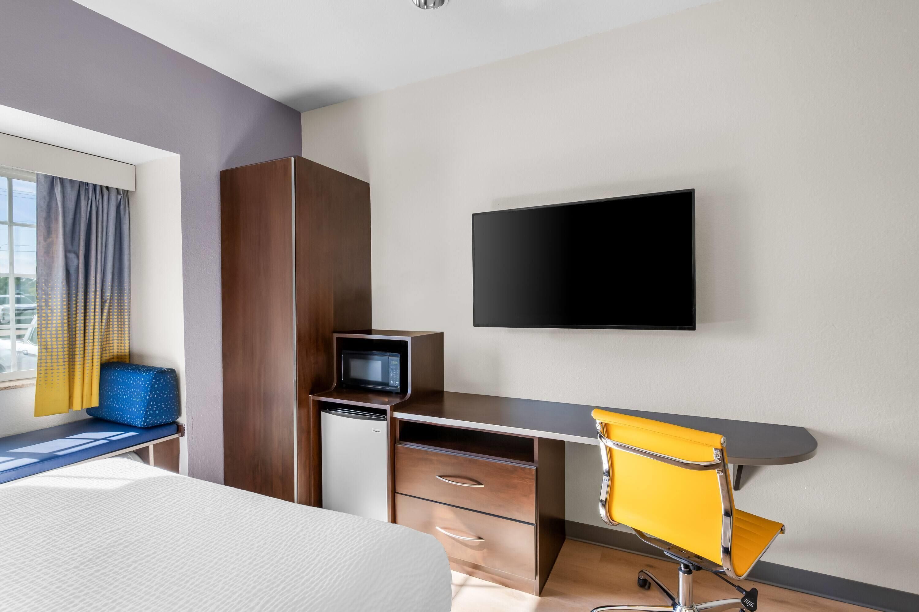 Hotellihuone, jossa on sänky, työpöytä tuolilla, televisio ja ikkuna, jossa on verhot.