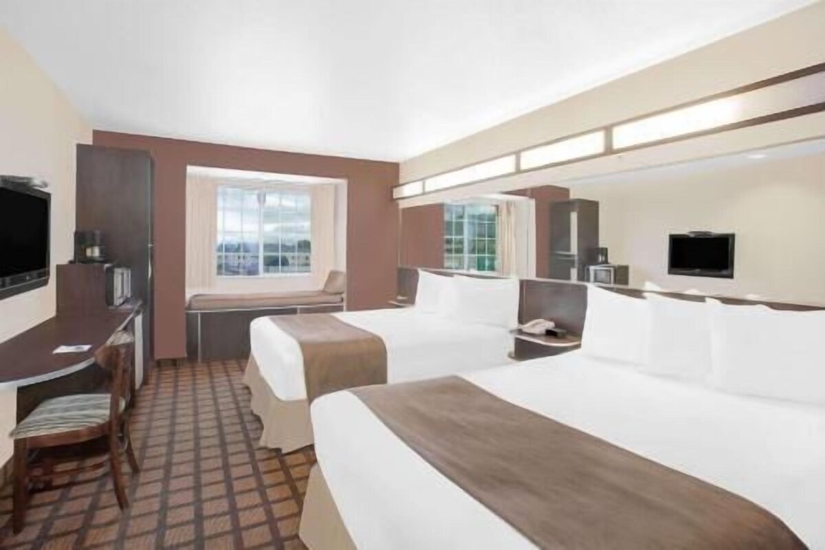 Habitación de hotel con dos camas, un escritorio, una silla, un televisor y una ventana.