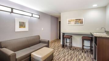 Ein kompaktes Hotelzimmer mit einer Sitzecke, einem kleinen Tisch, einer Küchenzeile und zwei Barhocker.