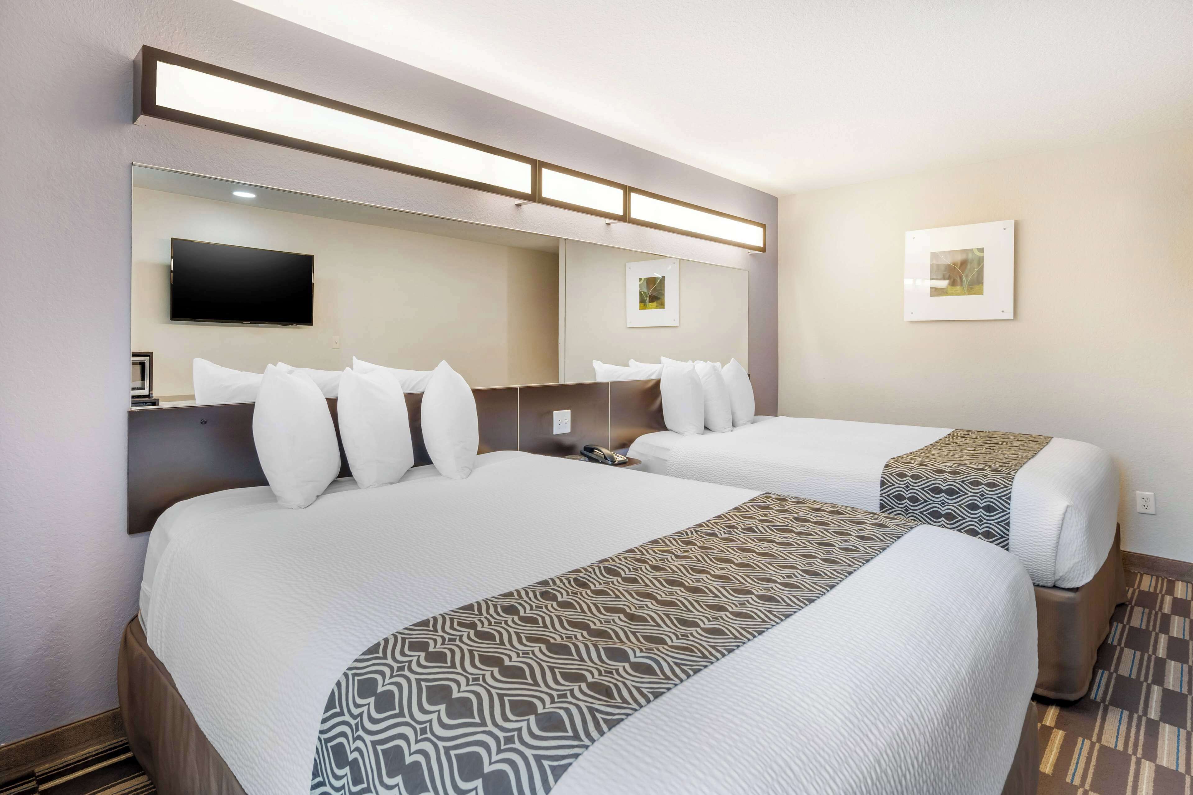 A hotel room with two beds, a flat-screen TV mounted on the wall, and a framed picture on the wall.