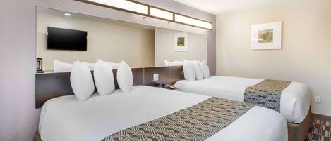 A hotel room with two beds, a flat-screen TV mounted on the wall, and a framed picture on the wall.