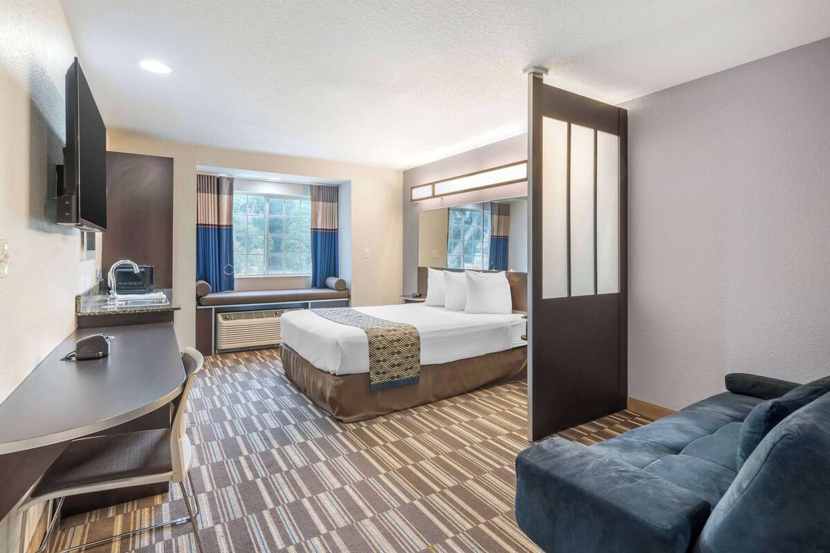 A hotel room with a bed, a desk, a TV, a window with curtains, and a sofa.