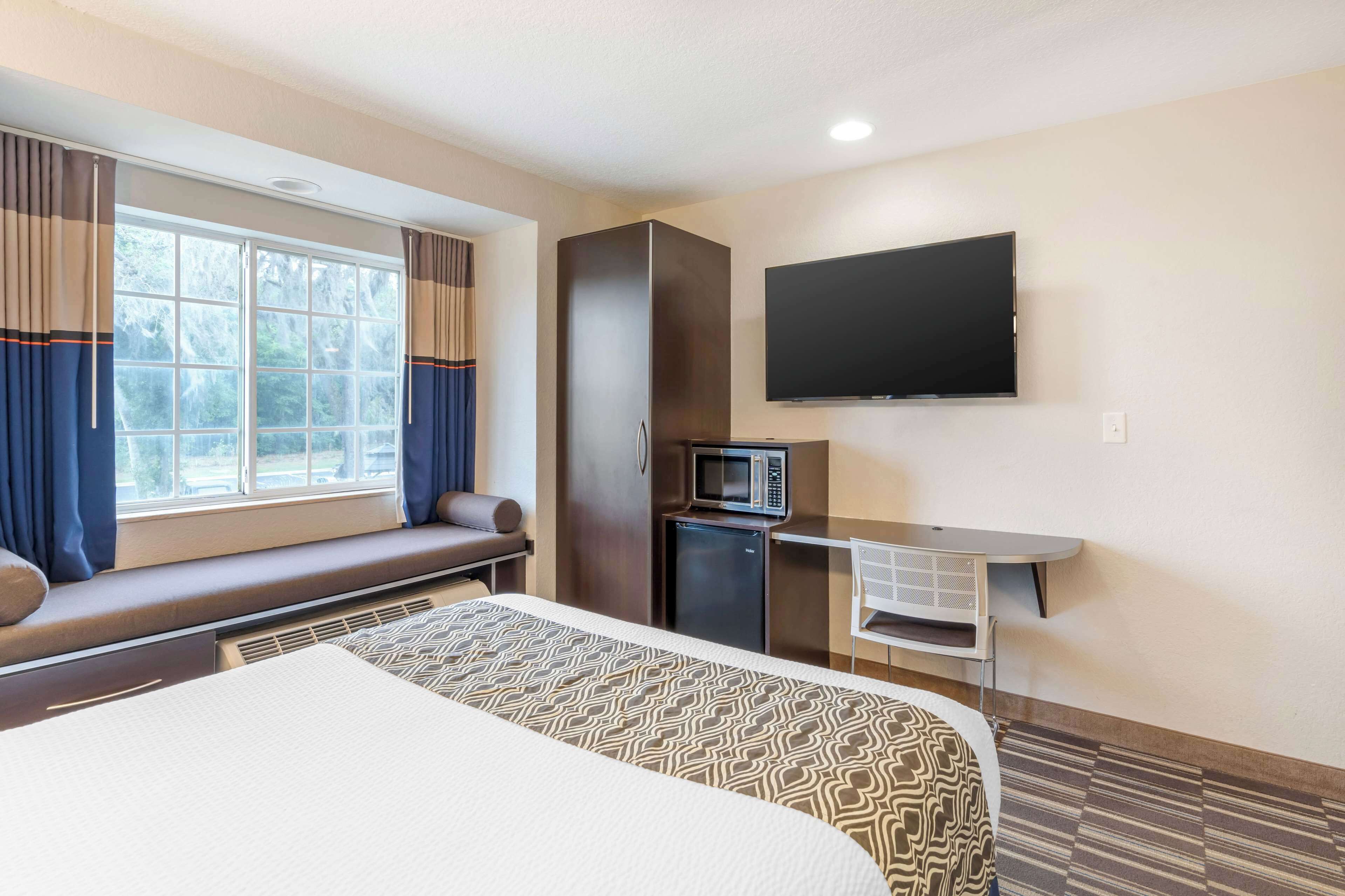 A hotel room with a bed, a desk with a flat-screen TV, a microwave, and a small refrigerator.