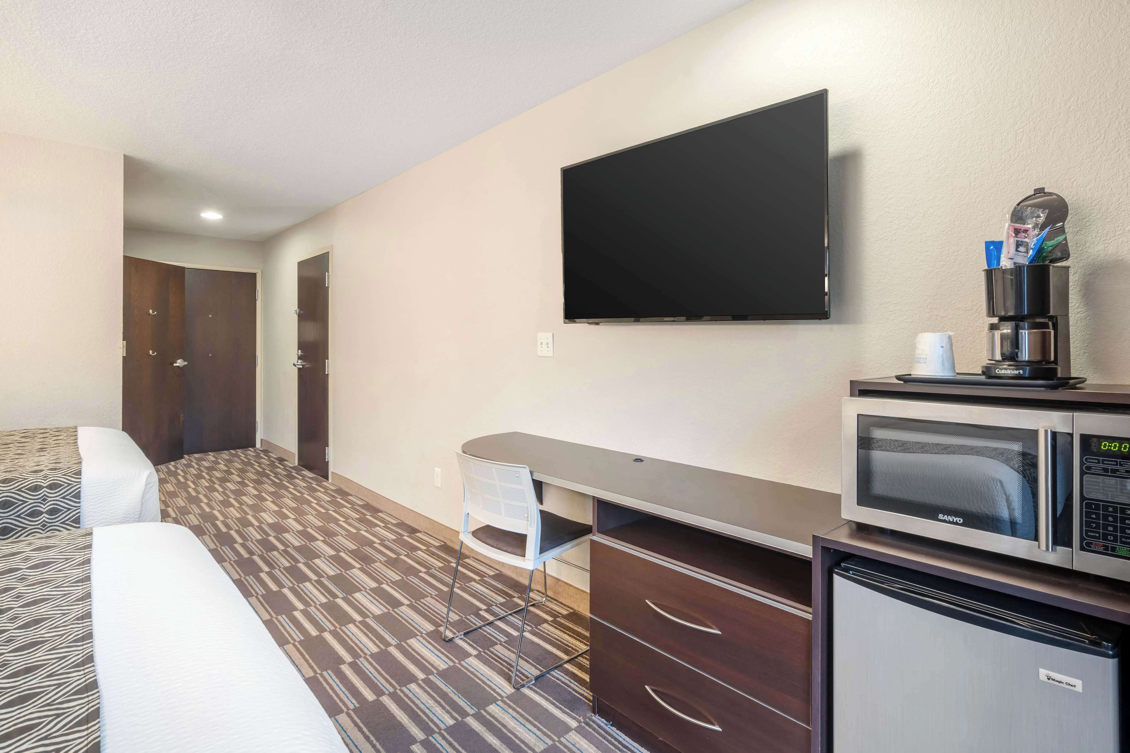 A hotel room with a bed, a desk with a microwave, a television, and a minibar.
