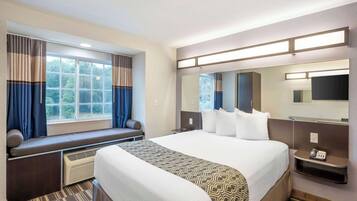 A hotel room with a large bed, a built-in bench with a seat cushion, a large mirror, a flat-screen TV, and a telephone on a bedside table.