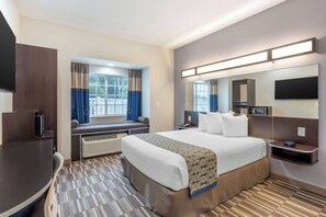 Una camera d'albergo con un letto grande, una scrivania, una sedia, una finestra con tende, una televisione a schermo piatto, uno specchio e uno scaffale a parete.
