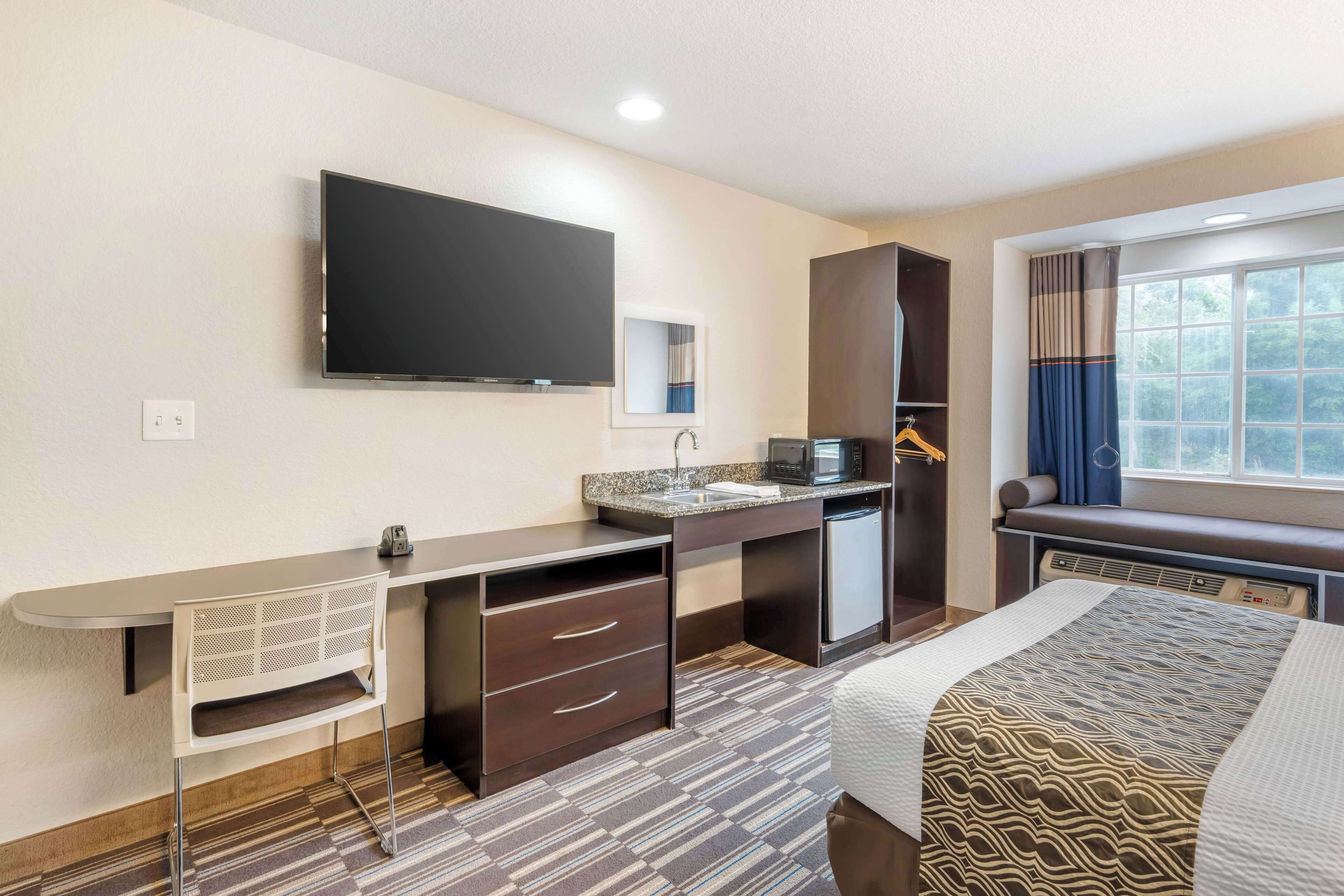 Une chambre d’hôtel comprenant un lit, un bureau avec un téléviseur à écran plat, un four à micro-ondes et une petite kitchenette.