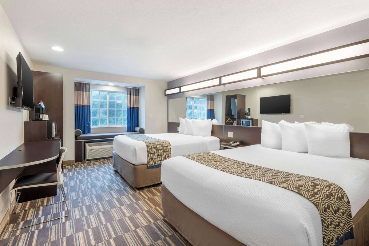 A hotel room with two beds, a desk, a TV, a window with curtains, and a mirror.