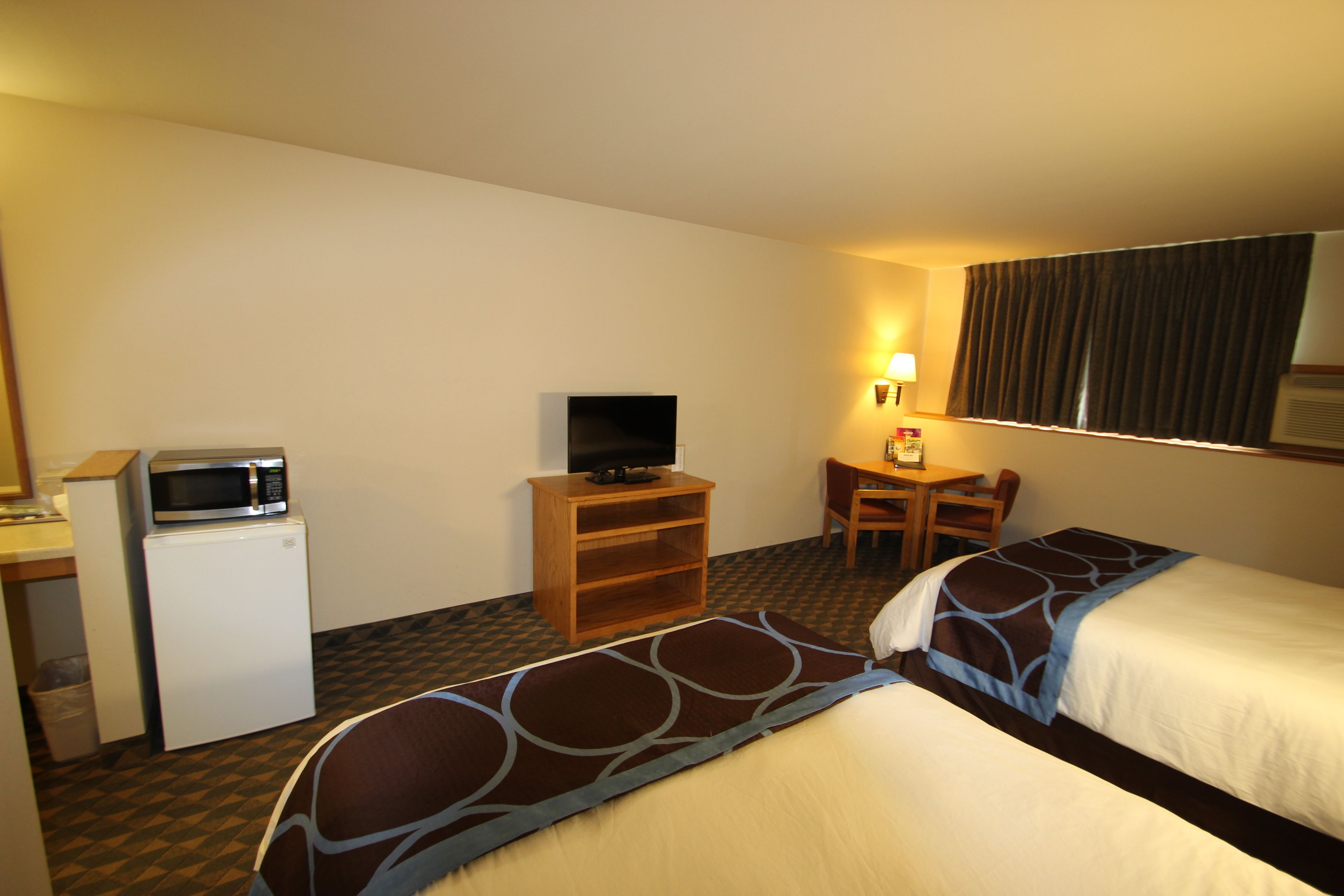 Habitación de hotel con dos camas, un escritorio con silla, microondas y televisión.