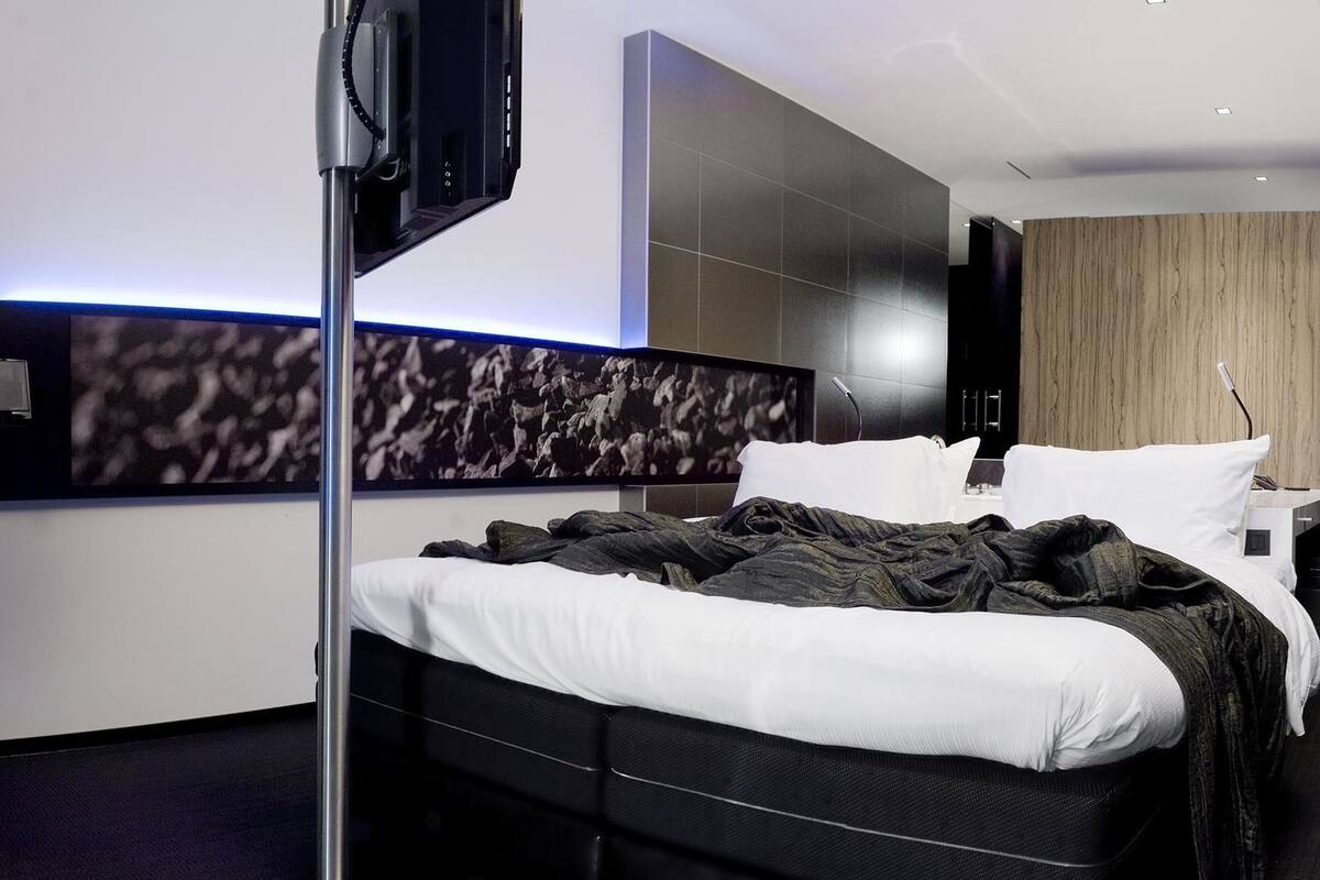 A modern hotel room with a large bed, a flat-screen TV mounted on the wall, and a wooden accent wall.