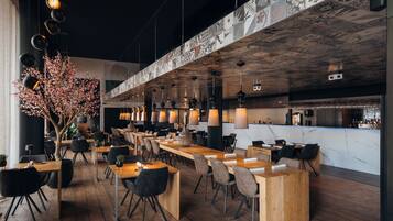 Een modern restaurant met houten tafels en stoelen, hangende pendantlampen en een decoratief plafond.