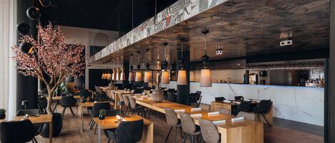 Un restaurant moderne avec des tables et des chaises en bois, des luminaires suspendus et un plafond décoratif.