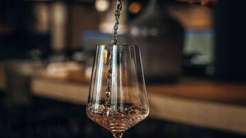 Una copa siendo llenada con un líquido, probablemente una bebida, en un ambiente con poca luz y un fondo desenfocado.