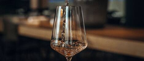 A glass being filled with a liquid, likely a beverage, in a dimly lit setting with a blurred background.