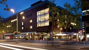 Un hotel moderno con fachada de vidrio, asientos exteriores y una entrada bien iluminada.
