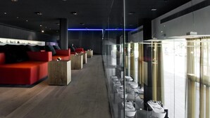 Un moderno vestíbulo de hotel con recepción, asientos con sofás rojos y un separador de vidrio con mesas y sillas para comer.
