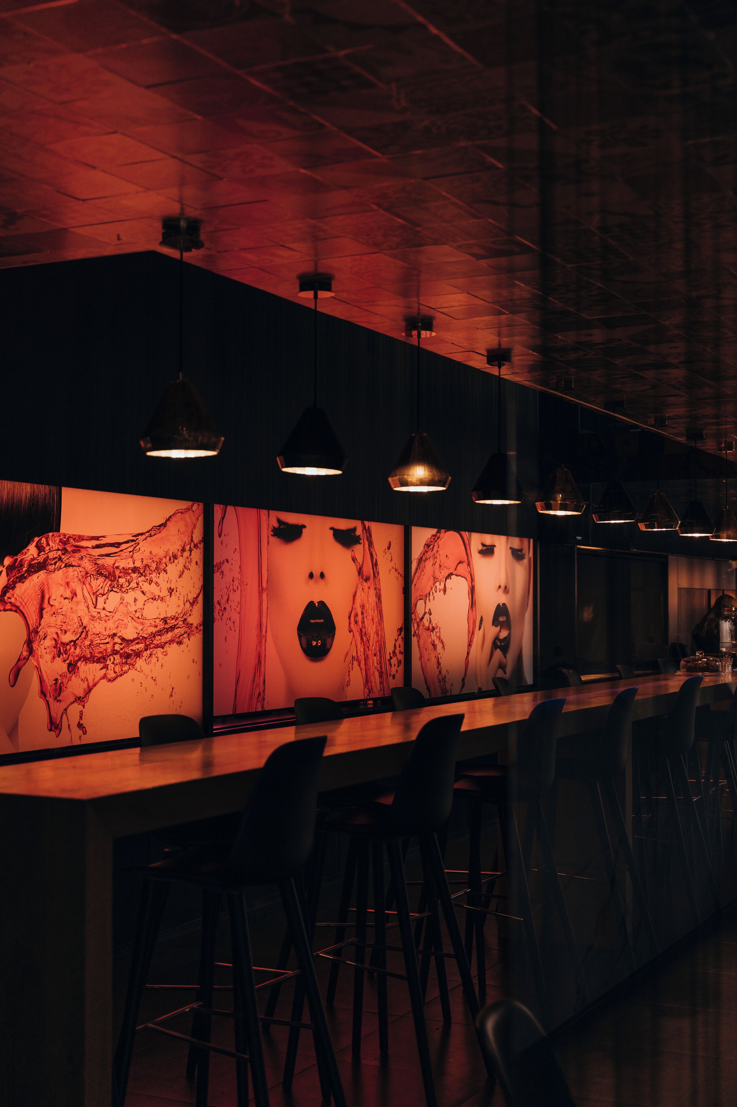 A bar area with a long counter, multiple hanging pendant lights, and bar stools.