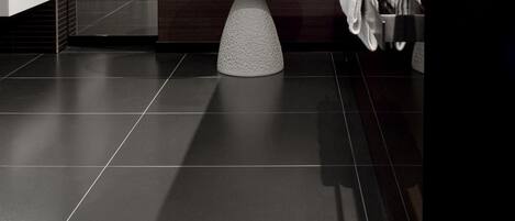 Un baño moderno con un lavamanos pedestal redondo, suelo de baldosas oscuras y una pared de acento de madera.