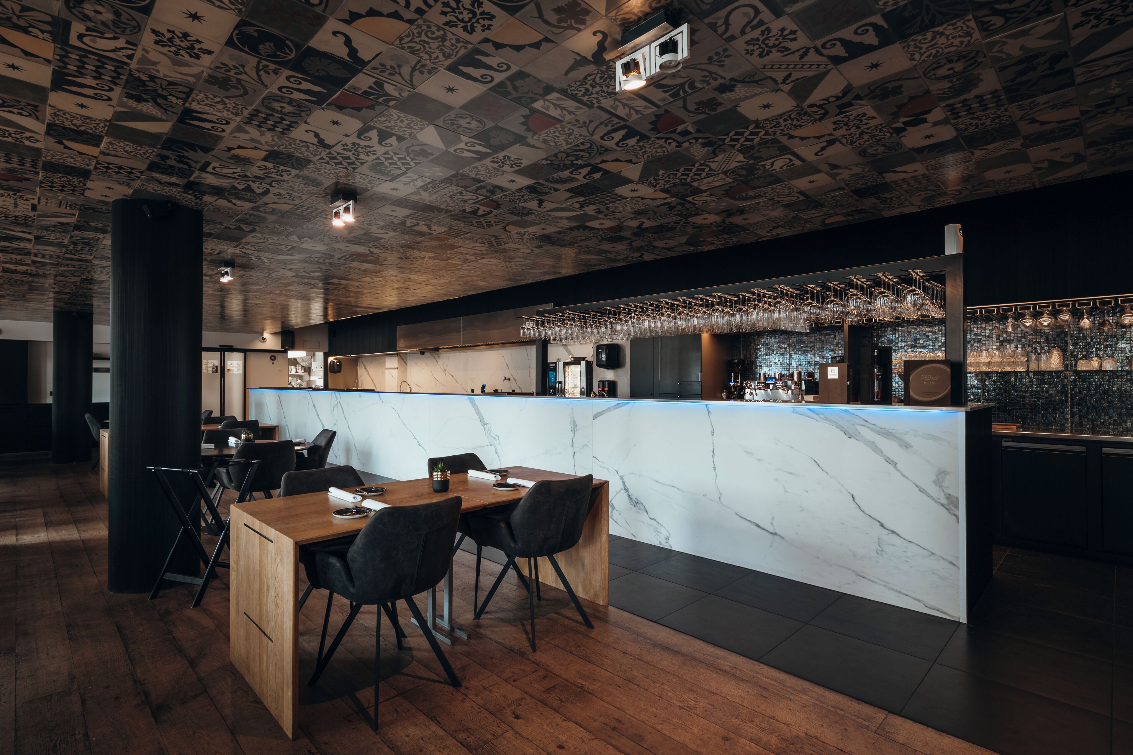 Een moderne bar met een marmeren aanrecht, zwarte stoelen en een plafond met artistieke patronen.