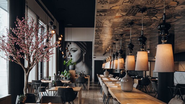 Un restaurante moderno con mesas de madera largas, sillas negras y lámparas colgantes.