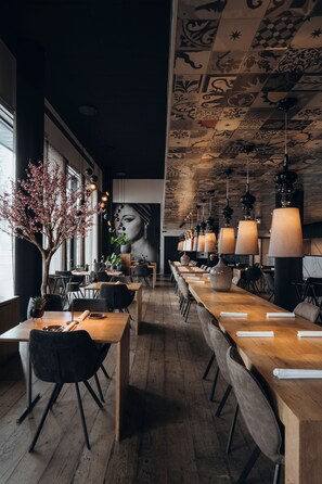 A modern restaurant with long wooden tables, black chairs, and hanging pendant lights. - Carbon Hotel - Different Hotels (Genk)