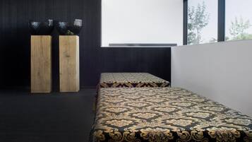 Une chambre moderne avec deux lits, des tables de chevet en bois et une grande fenêtre laissant entrer la lumière naturelle.