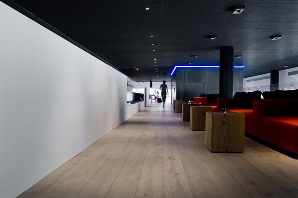 A modern interior with a wooden floor, red seating area, and a person walking down a corridor. - Carbon Hotel - Different Hotels (Genk)