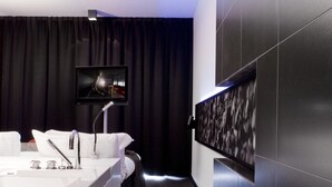 Un baño moderno con un espejo grande, un lavamanos y un televisor montado en la pared.