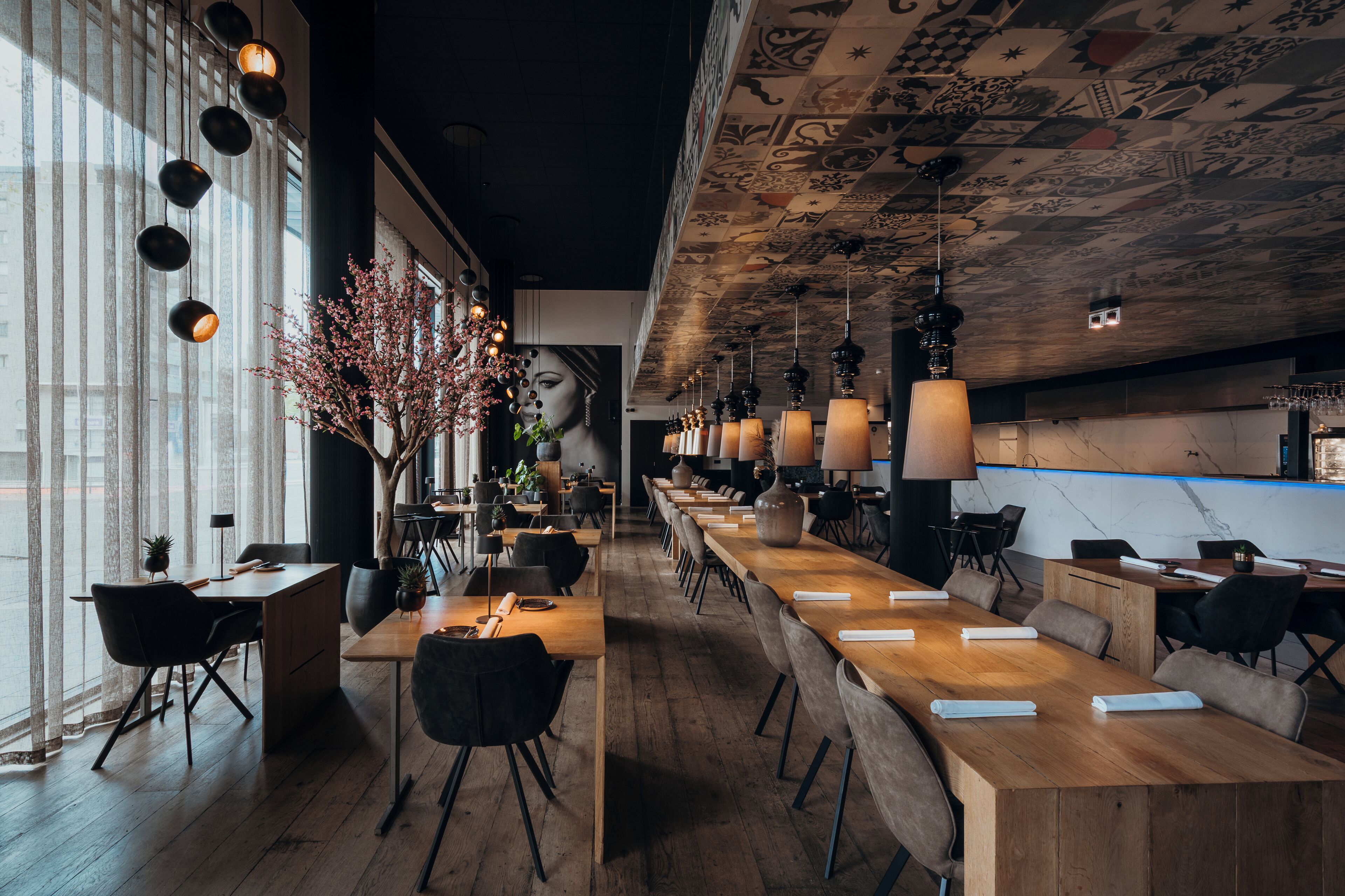 Un restaurante moderno con mesas de madera largas, sillas negras e iluminación colgante.