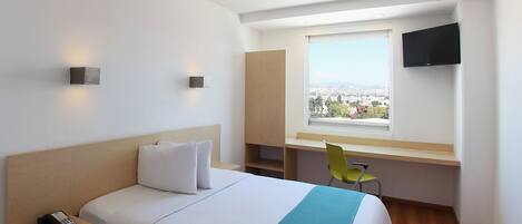 Habitación de hotel con cama, escritorio, silla, televisión y ventana con vista a la ciudad.