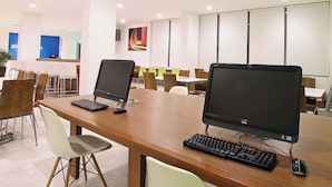 Una sala de conferencias con dos amplios escritorios, cada uno con un monitor de computadora, teclado y ratón. La sala presenta un diseño moderno con mesas y sillas de madera, y un gran ventanal al fondo.