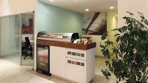 Un área de recepción con un mostrador refrigerado, una zona de estar con una silla y una planta en maceta.