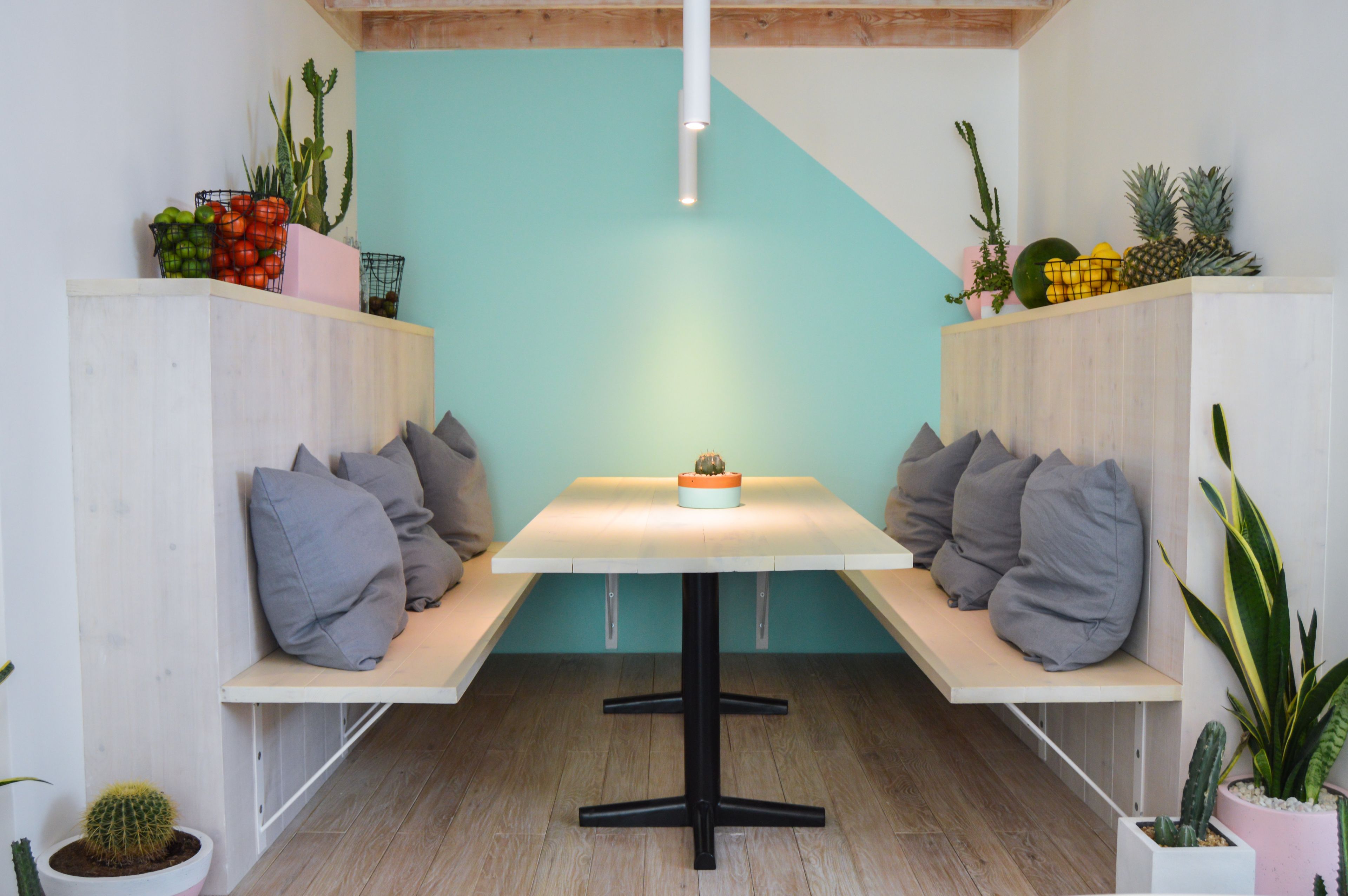 Een moderne eetruimte met een witte tafel en bankjes, omringd door potplanten en een wand in teal blauw.