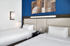 Habitació d'hotel amb dos llits, una tauleta de nit amb un telèfon, una làmpada penjada a la paret i un quadre abstracte gran.