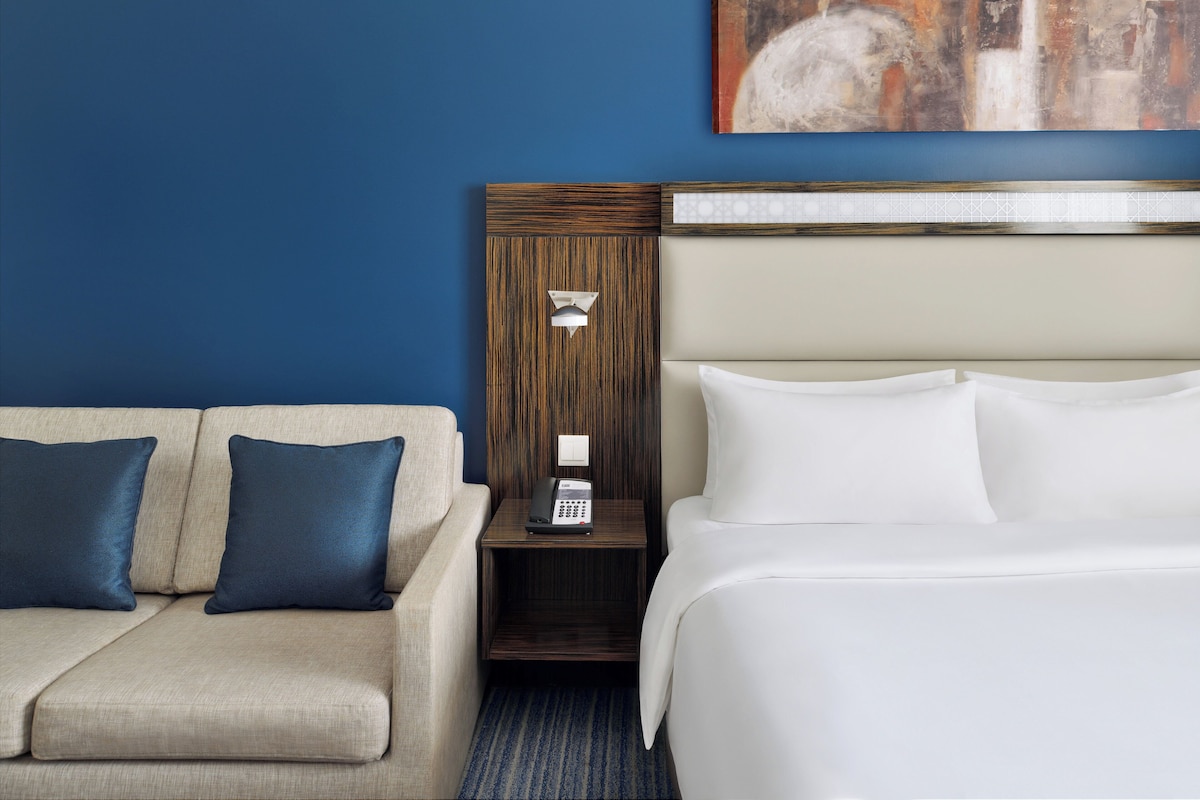 Una habitación de hotel con cama, sofá y mesita de noche con teléfono.