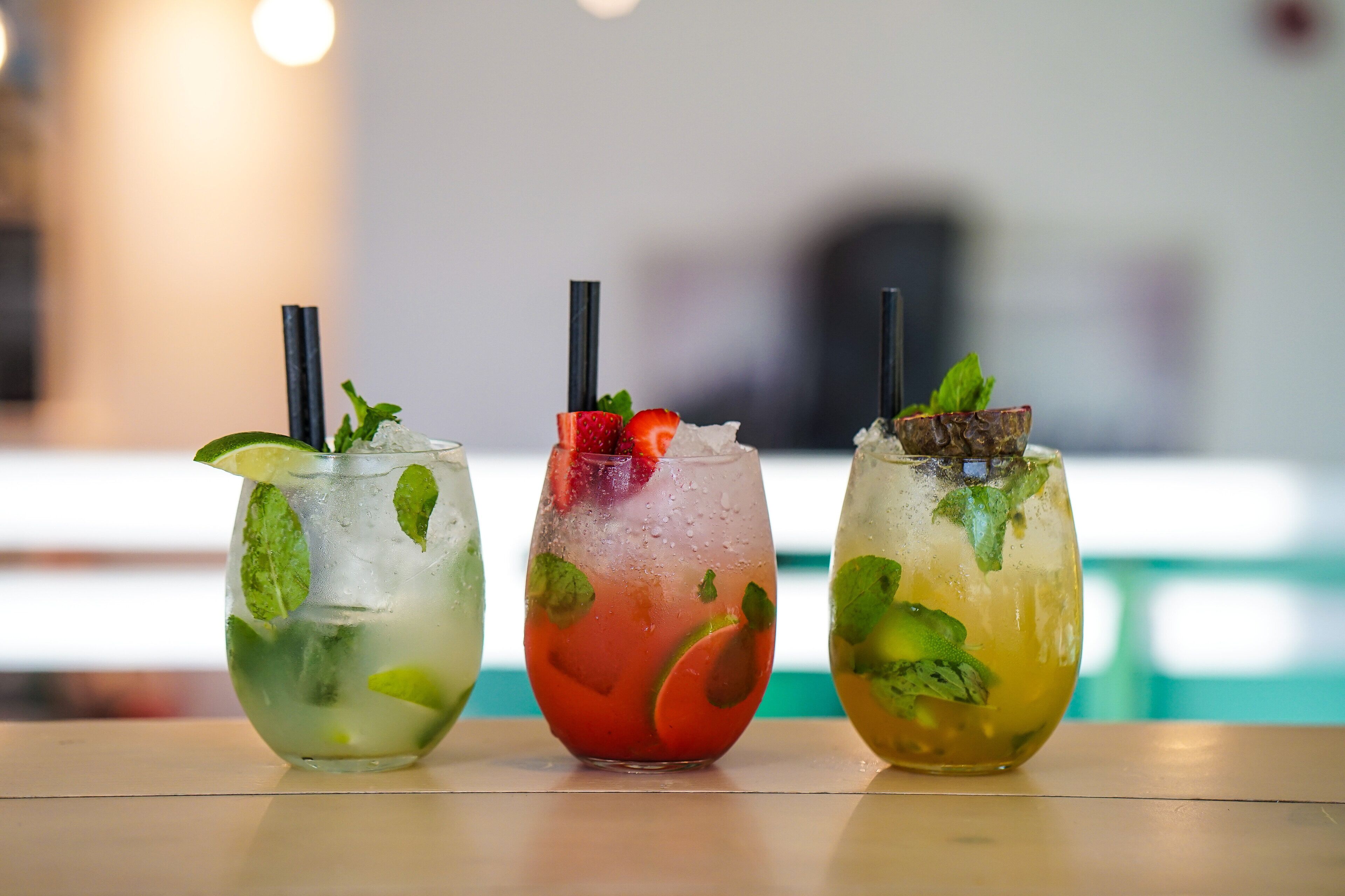 Três cocktails com folhas de hortelã e guarnições de frutas sobre uma mesa.