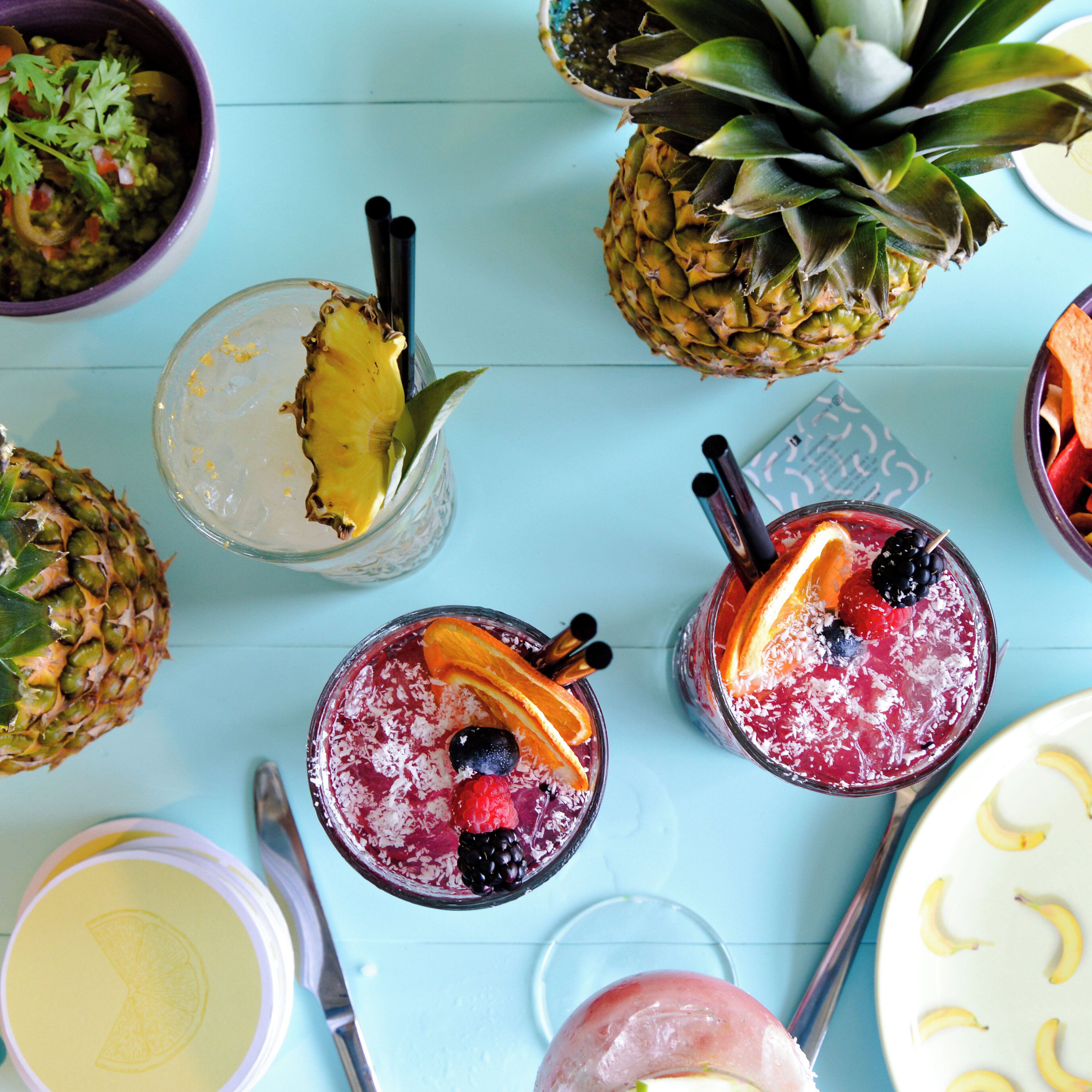 A variety of tropical drinks and fruits on a light blue surface.