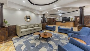 Un vestíbulo de hotel con un sofá, sillones azules, un mostrador de recepción y una alfombra estampada.
